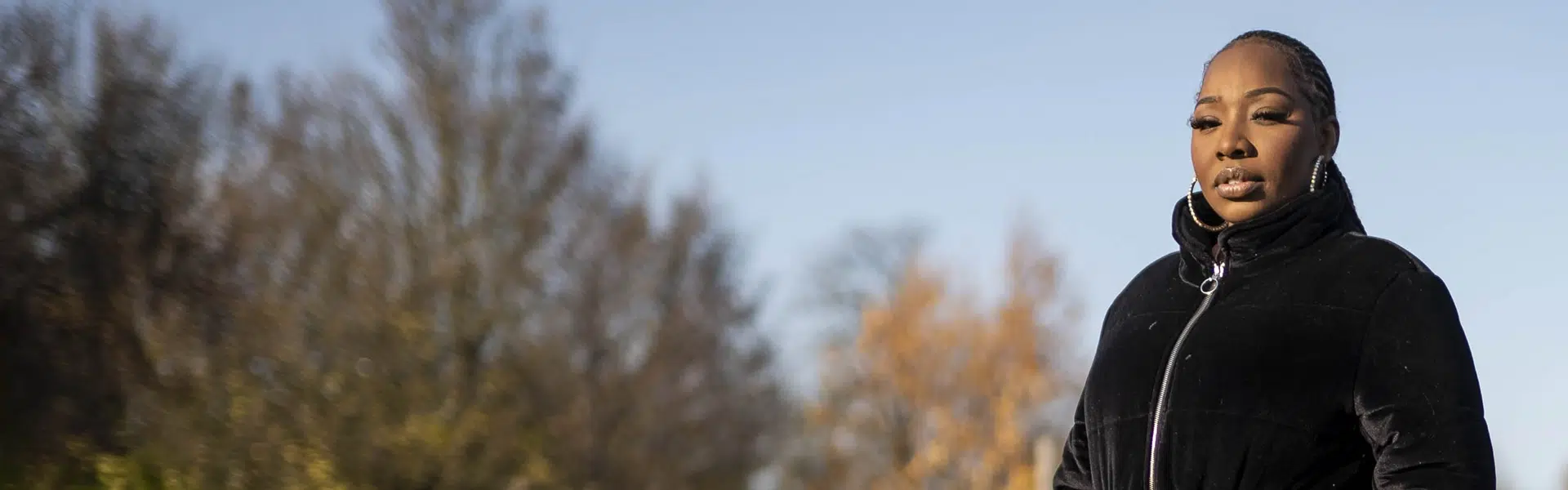 A woman standing outside in a park. she looks thoughtful