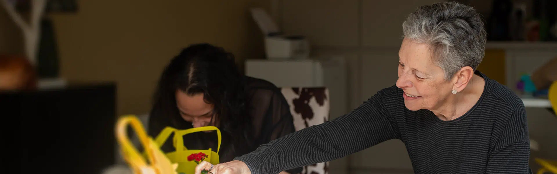 A woman sitting with a young female resident doing crafts