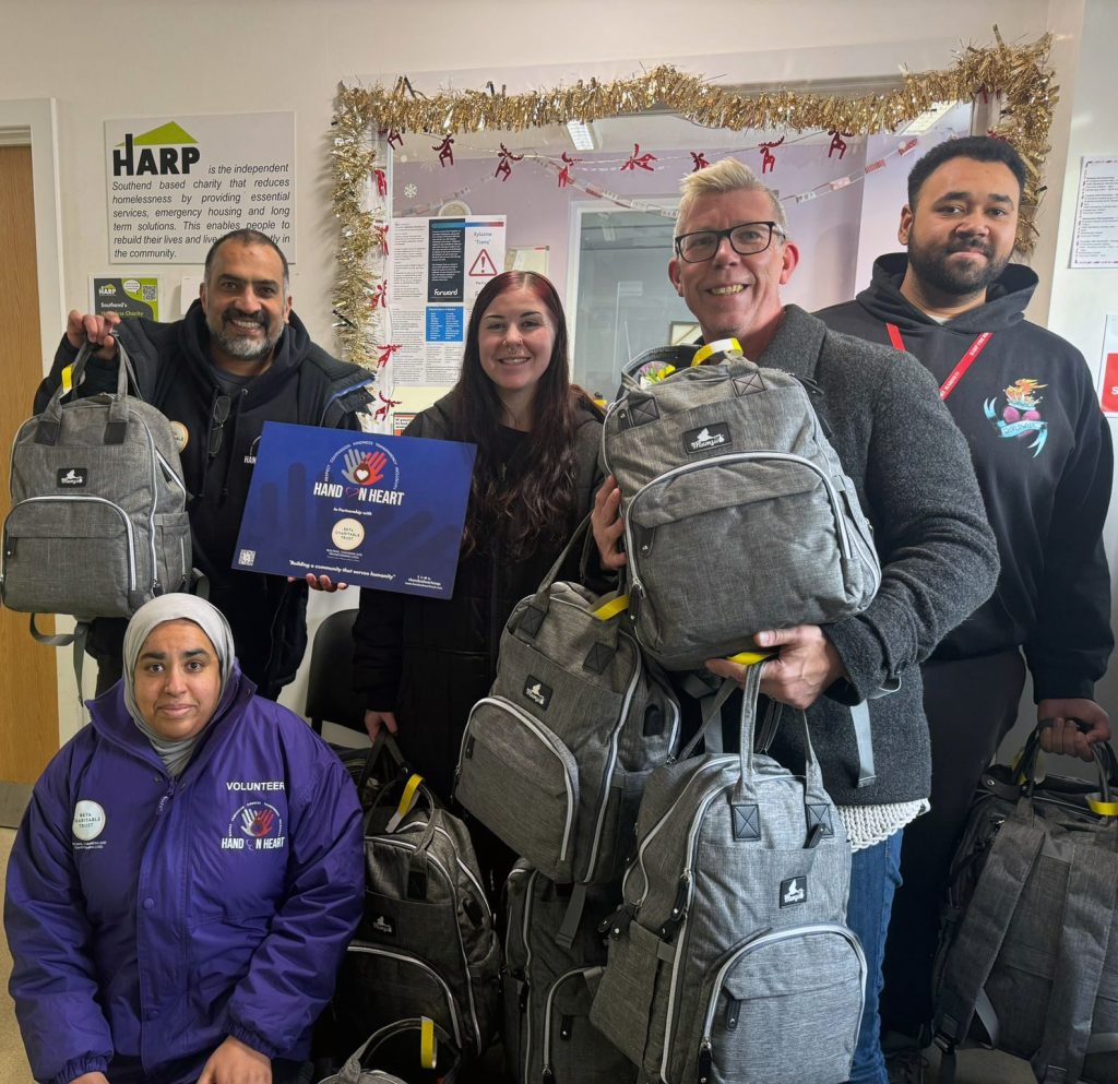 3 staff from HARP accept donations of back packs from two volunteers with Hand on Heart